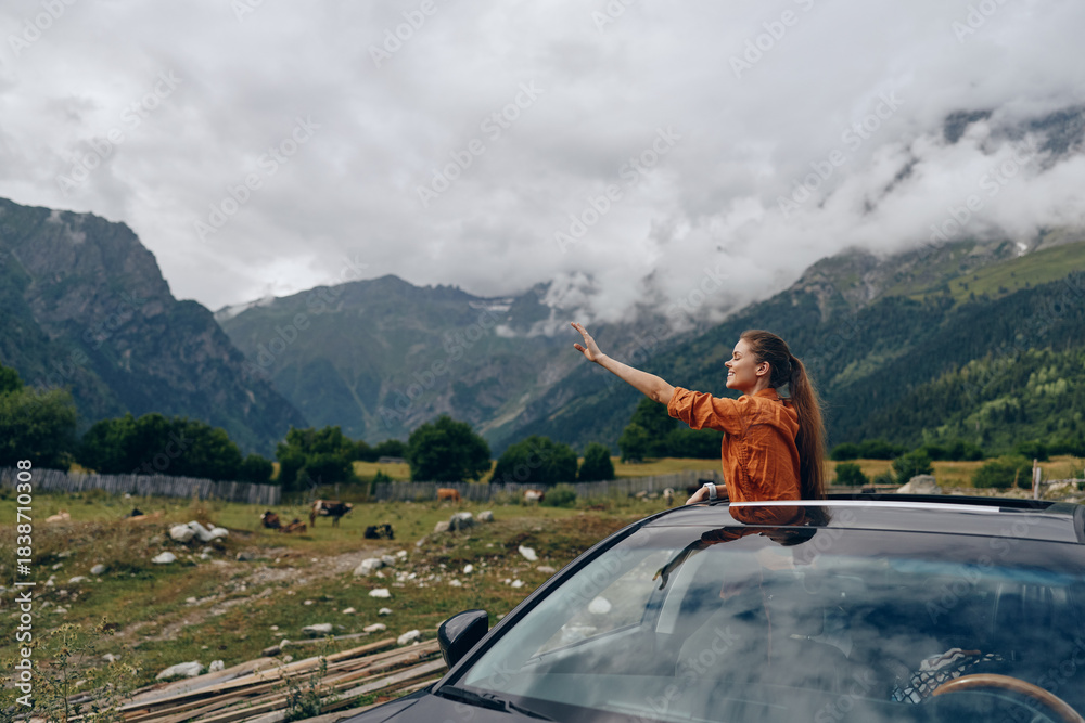 Fototapeta premium A woman leans from a sunroof of a car in a rural valley, pointing toward distant mountains, capturing a moment of adventure, freedom, and exploration in open countryside