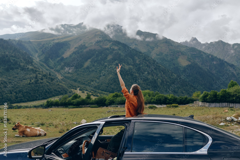 Fototapeta premium woman car mountains meadow cow roadtrip nature travel sunroof, woman standing through sunroof in meadow with cow and peaks, authentic inclusivity joyful freedom relaxed smile