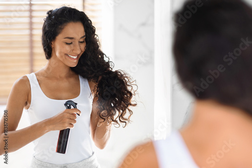 Bilde på lerret In a well-lit bathroom, a woman with curly hair enjoys applying a curl enhancing spray