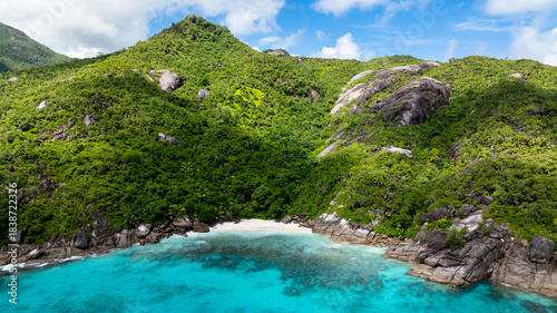 A small, secluded sandy beach bordered by lush green hills, leading to clear turquoise waters. Seychelles, Mahe.