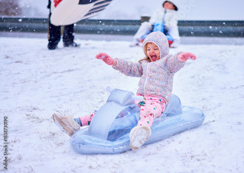Joyful Children Sledding Down a Snowy Hill - Winter Fun and Laughter on Inflatable Sleds. Winter Thrill Ride