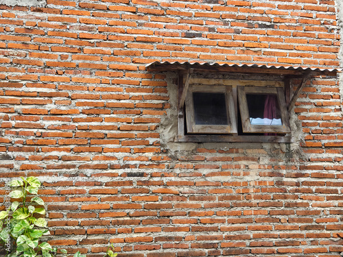 Old rustic brick wall with a small wooden window and worn roof tiles in natural daylight