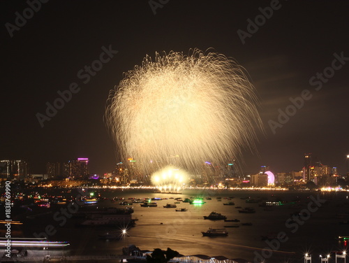 Fireworks lighting up the night sky in Pattaya, creating a vibrant and colorful display over the city and ocean. The bright explosions illuminate the coastline, capturing the festive atmosphere of thi