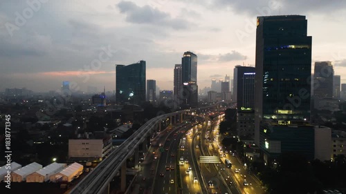 Night Aerial View of Jakarta's Illuminated Skyline and Heavy Traffic Flow on Elevated Highway and LRT Track