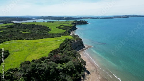 Drone aerial flight toward the coastal cliffs and bright shoreline of Long Bay in Auckland New Zealand.