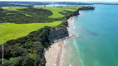 Drone aerial orbit revealing the dramatic cliffs and bright coastline of Long Bay in Auckland New Zealand.