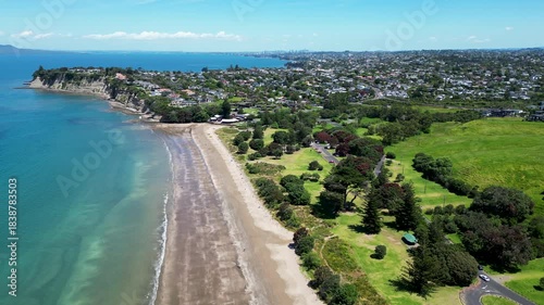 Drone aerial view of Long Bay beach with blue water and coastal parkland in Auckland New Zealand.