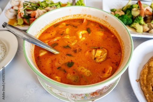 Traditional Thai spicy tom yum seafood soup with shrimp and mushrooms in white bowl.