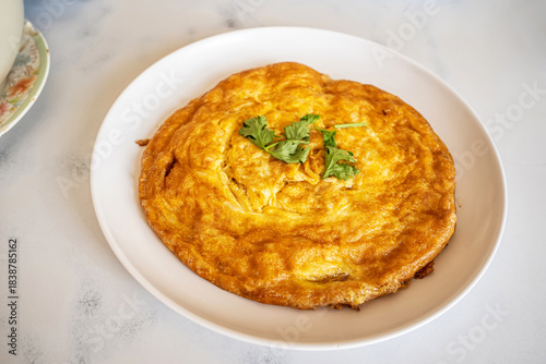 Golden brown Thai style fluffy omelet with coriander topping served on white plate.