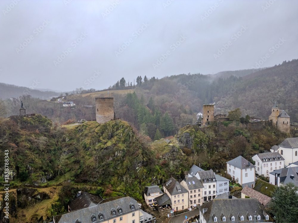 Obraz premium Esch-Sur-Sure, Wiltz, Grand Duche De Luxembourg, December 7, 2025, Castle Ruins Perched Atop Rugged Cliff Overlooking River And Village, Weathered Towers And Mossy