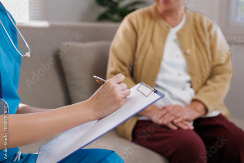Nurse providing home care, writing on a clipboard during a health check up with an elderly patient at home