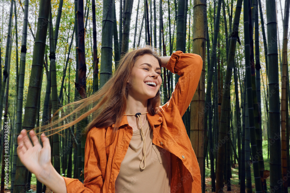 Fototapeta premium Woman smile bamboo forest portrait nature joy outdoors, young woman in orange shirt laughing with eyes closed among tall bamboo stalks, carefree motion, lifestyle, travel and wellness.