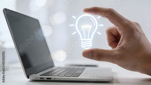 Hand holding glowing light bulb near laptop