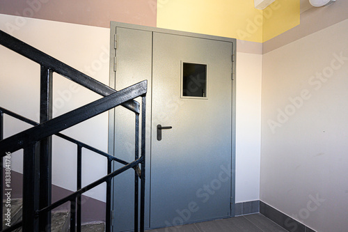 Secure metal door, staircase with black railing, interior walls in neutral colors, creating a functional and minimalist design for a commercial or institutional space