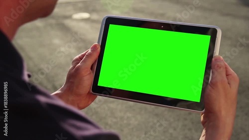 Person holding a tablet computer with a green screen, ready for chroma key compositing and digital content integration in outdoor setting