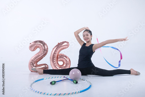 Φωτογραφία Rhythmic gymnast girl performs a ribbon twirling move, with other rhythmic gymnastics equipment and a number 26 balloon placed next to her