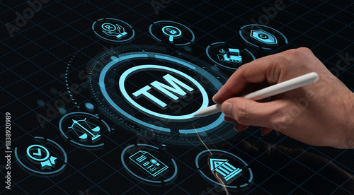 Hand holding digital pen touching holographic trademark icon on futuristic HUD interface with legal and copyright symbols on dark tech background.