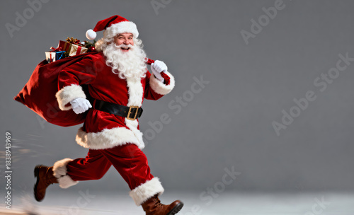 Jolly Santa Claus running with a sack full of Christmas presents, grey background. Text space