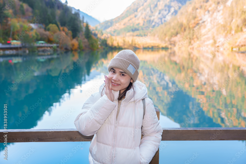 Fototapeta premium Happy woman traveler travel in jiuzhaigou national park in Sichuan, China. Tourist sightseeing Panda lake and snow mountain in Autumn season. Famous Landmark and Vacation near Chengdu, China