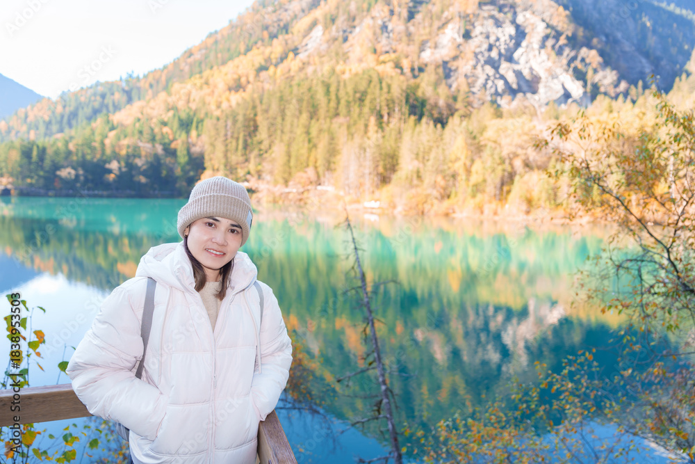 Fototapeta premium Happy woman traveler travel in jiuzhaigou national park in Sichuan, China. Tourist sightseeing Arrow Bamboo lake and snow mountain in Autumn season. Famous Landmark and Vacation near Chengdu, China