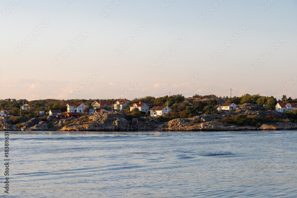 Fototapeta premium Vrango, Sweden - 09-08-2025 A beautiful summer sunset over the island Vrango in the Gothenburg archipelago with a view on fishing cabins hiding behind a pier of big rocks to protect them from the tide