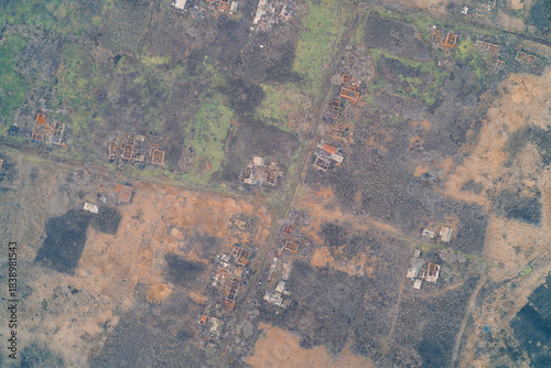 Aerial top down view of scattered ruined house foundations in destroyed village. War zone civilian settlement destruction and scorched earth landscape.