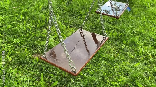 Outside swing set, close-up. Wet chains swing. Summer rainy day. Raindrops fall on the seat.