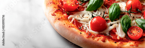 Fresh margherita pizza topped with melting mozzarella, cherry tomatoes, and basil leaves on a crisp crust against a light marble background.