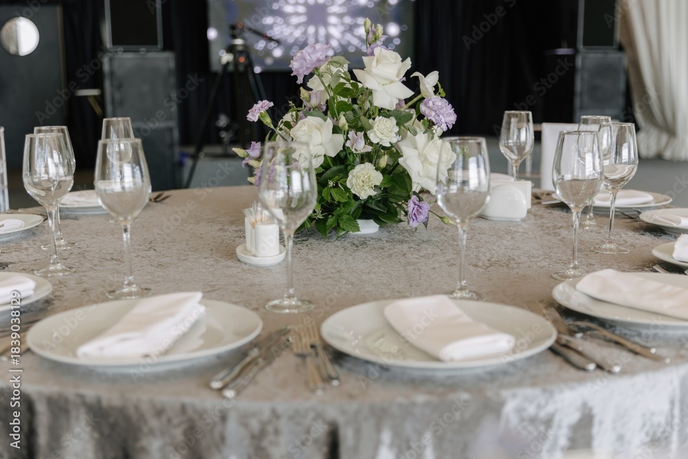 Fototapeta premium Elegant wedding table setting with grey tablecloth, white plates, crystal glasses and floral centerpiece of white roses