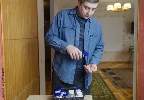 Man taking dietary supplements at home, pouring pills from a bottle and drinking with water. Concept of daily vitamins, health care and wellness routine.