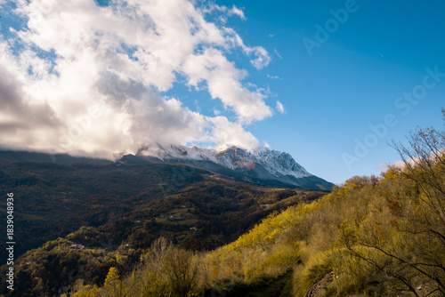 Snow capped mountain peaks emerging from clouds, an autumn landscape with colorful hillsides and clear blue sky