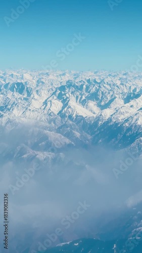 Winter Background. 4K Vertical view of snowy Himalayas and clouds as seen from airplane window. Frozen peaks during winter season in Kashmir, India. Aerial shot of a snowy mountain range.