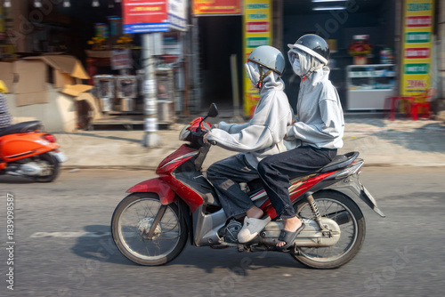 A couple in veiled clothing rides down a city street, Vietnam