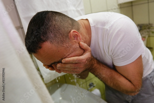 Man washing face, hygiene and skincare with water, basin and grooming during morning routine. Male person in bathroom, cleaning skin with hands and cleanliness, wellness and self care.