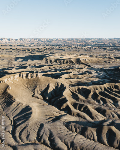 Aerial view of the Moon Overlook Road landscape, where stark, stratified rock formations carve deep shadows under the clear sky, Utah, United States.