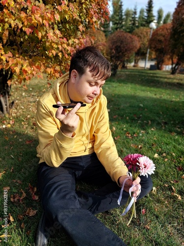 A sad guy with a bouquet of flowers in an autumn park.