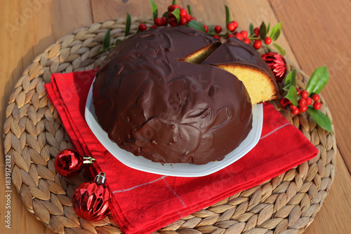 Italian traditional sweet cake called Parrozzo made with almonds and semolina on a plate on wooden table with Holly branches with red berries and red Christmas glass balls with copy space