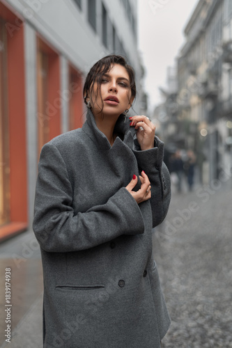 .Cheerful brunette woman in stylish coat with crossbody walking in urban street.	