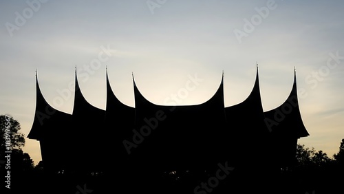 Silhouette of a traditional Minangkabau house against a sunset sky.