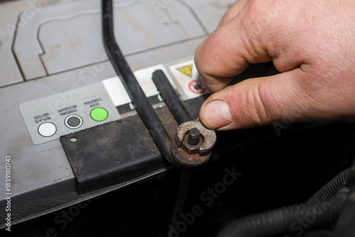Εκτύπωση καμβά A close-up captures a hand tightening a nut on a metal retainer that secures the car battery to its compartment, illustrating the installation process