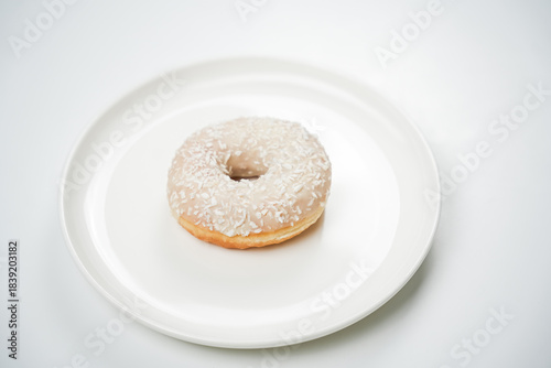 Fotografía A donut with a smooth glaze and coconut flakes is placed on a white plate