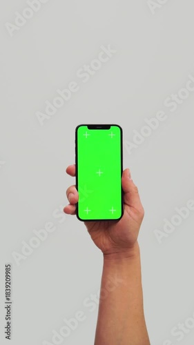 Male hand using chroma key smartphone on White background. Blank green screen mock up with Tracking Markers. Hand lifts phone up