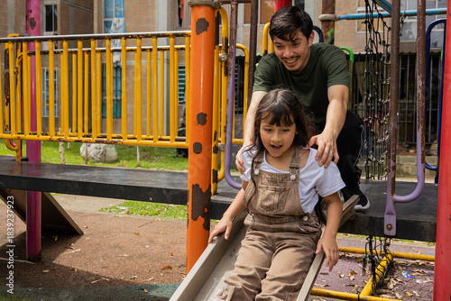 Man cheerfully helping his niece slide down a playground slide in the park, a tender and fun outdoor family scene