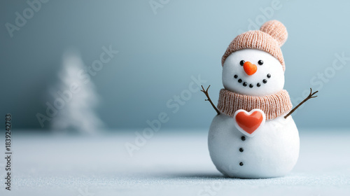 Christmas snowman with orange carrot nose and heart decoration wearing knitted hat in winter landscape, joyful holiday scene