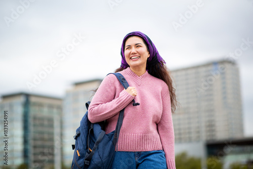 Happy Asian woman walking with backpack in cityscape background