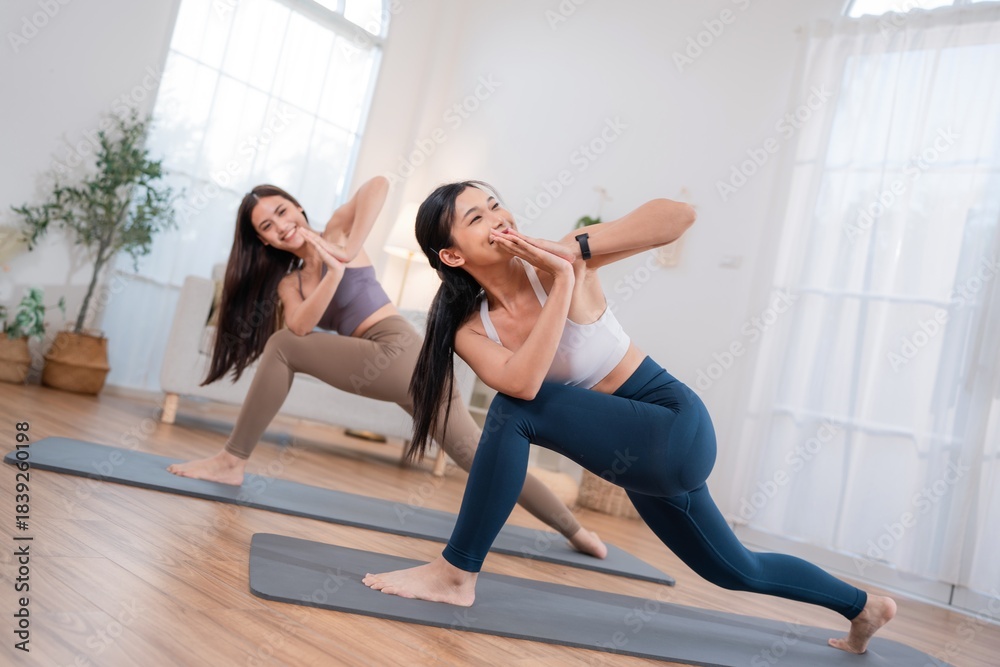 Obraz premium Two women practice yoga in a bright room with sunlight coming through large windows during a morning class