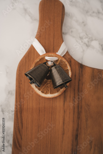 A charming display features two small bells resting on a dried orange slice, all artfully arranged on a wooden serving board. This adds warmth and character to any setting