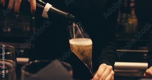 close-up view of woman's hand hold bottle pouring champagne into glass. serving alcoholic drink in restaurant. bartender pours champagne. air bubbles close up in glass. foam from sparkling wine 