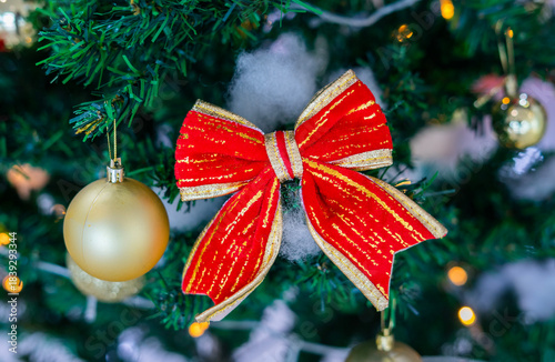 Festive Christmas ornaments hanging on a snowy pine tree. Glittery red and silver baubles, a gold and red bow, a snowman and a bell decorate the frosted green branches.