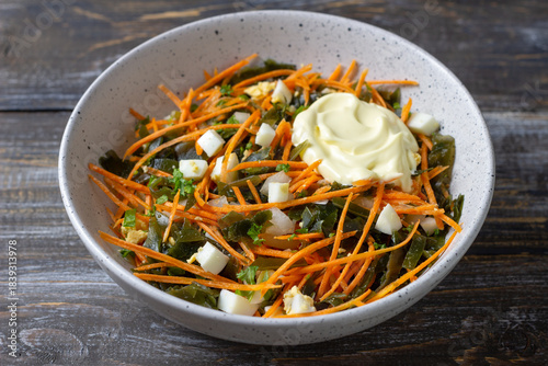 Seaweed and carrot salad with diced egg and dollop of creamy mayonnaise in ceramic bowl
